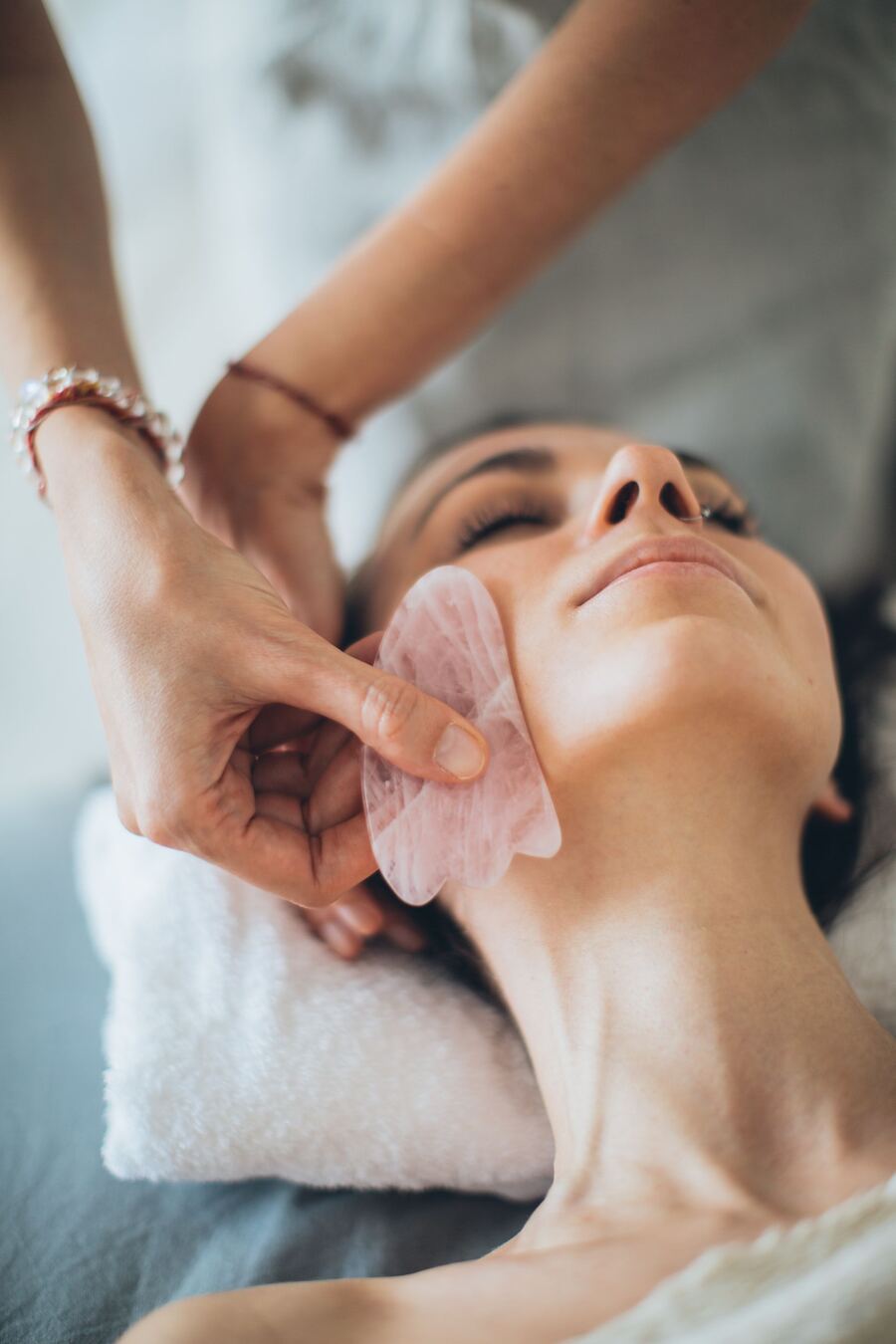 Practitioner gliding a rose quartz gua sha stone along the jawline during facial rejuvenation