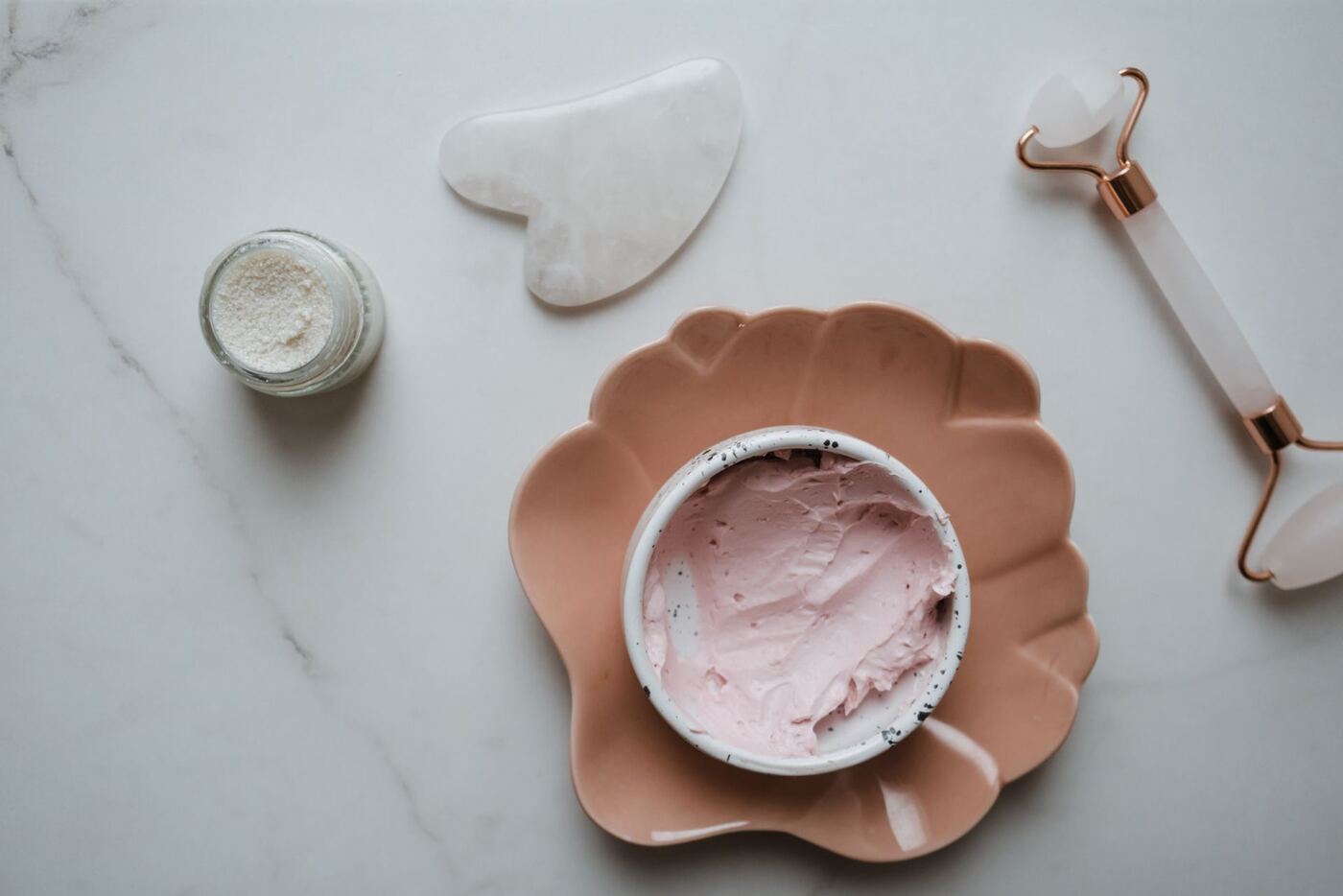 Jade and rose quartz gua sha tools with a facial roller on a marble surface